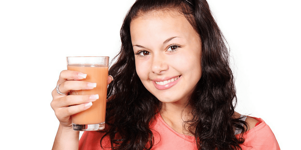 Curly woman wearing an orange dress smiling holding a glass of juice in white background