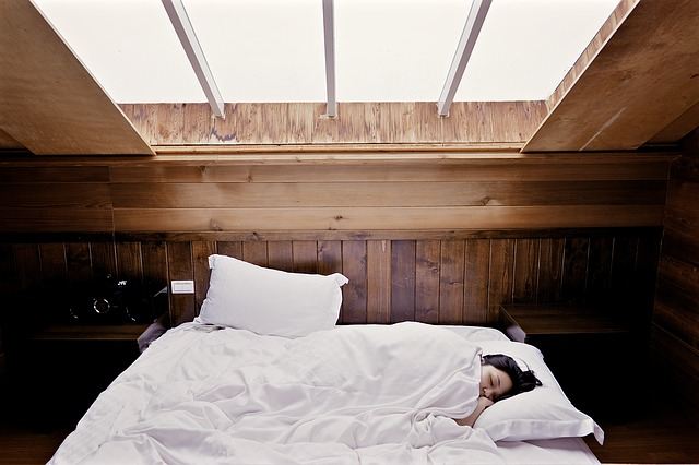 Woman sleeping in the white bed inside a wooden room with glass at the center of the ceiling.