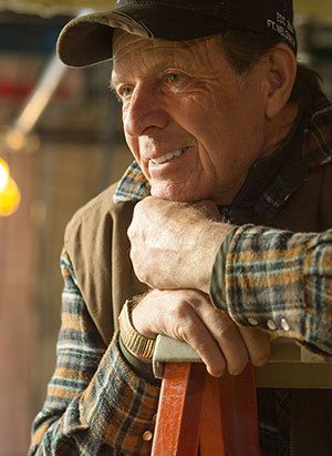 Gary, founder of Young Living leaning on the wooden chair. An old man wearing a cap, and a checkered long sleeve polo