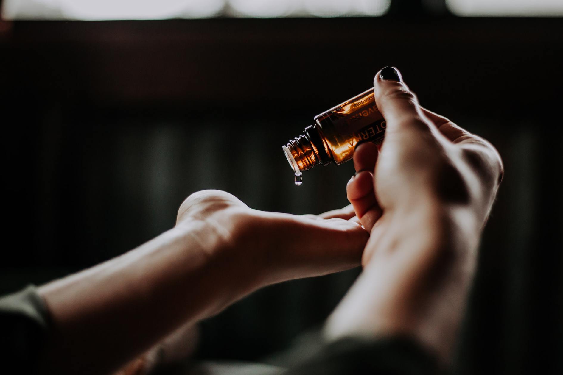 Applying Doterra essential oil on the hands in dark blurry background.