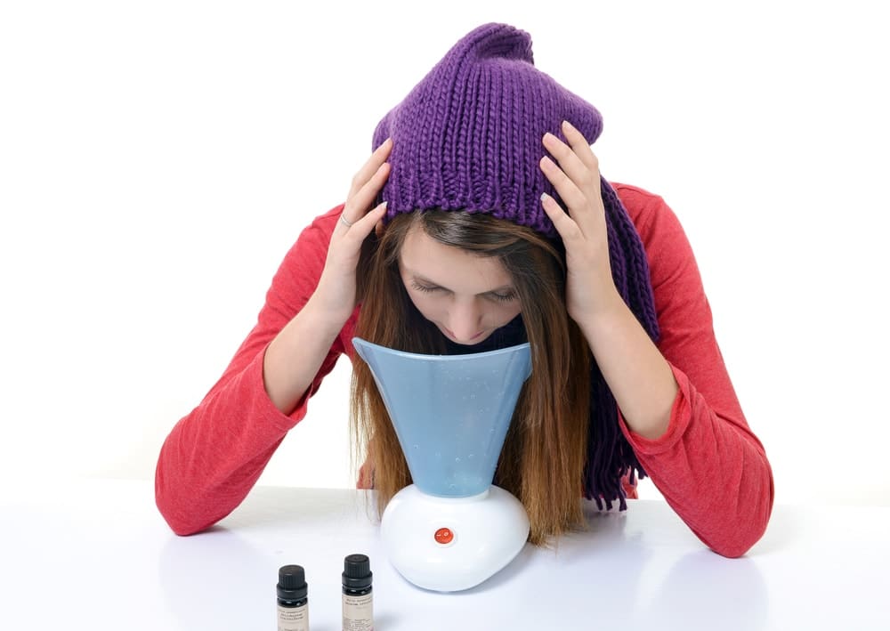 Young woman inhaling from inhaling machine, essential oil bottles in white background