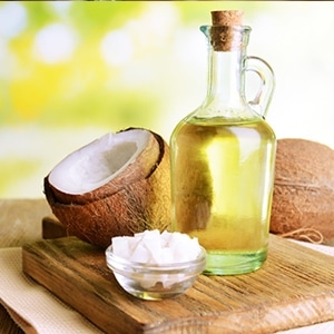 coconut shells, coconut chunk in a bowl, and coconut oil on a decanter or jar on a wooden chopping board
