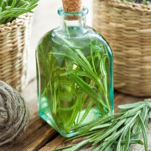 1 bottle of oil with Rosemary leaves inside, 2 knitted basket with rosemary leaves, rope, rosemary leaves below the bottle placed on the wood.