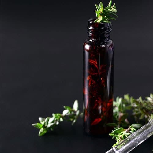 1 bottle of oil with thyme leaves, thyme leaves below the bottle, dropper in black background