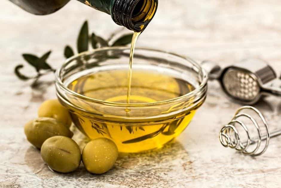 Olive Oil poured on a small bowl with olive fruit and oil presser on a background.