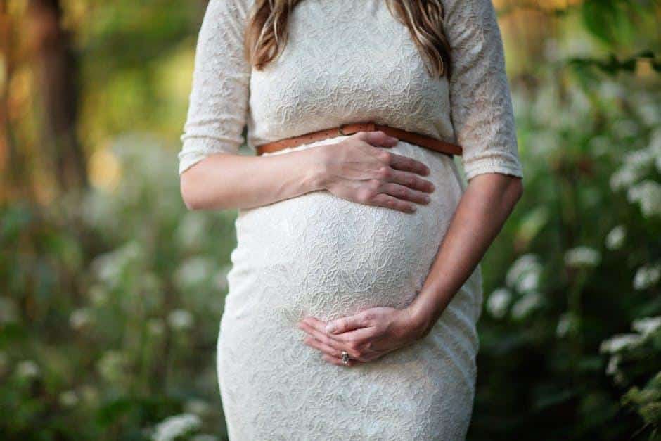 Pregnant woman holding her tummy in blurry green background.