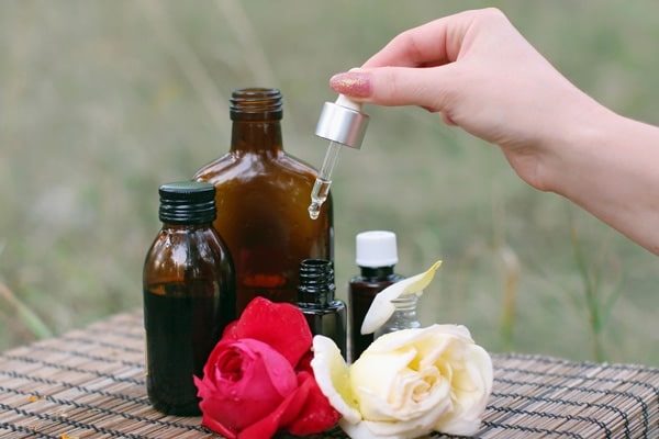 Adding drops of oil in an amber bottle in a table with other different sizes of essential oil bottles and roses