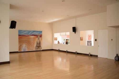 A studio. wooden floor, concrete white wall and ceiling, 2 large windows, a door, and a printed cloth in the wall, with speakers hanged on the wall.