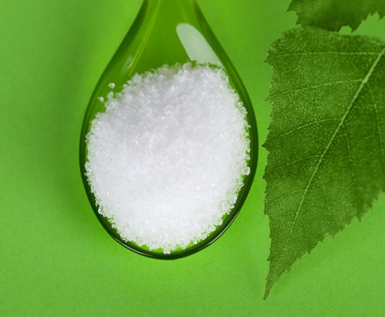 Xylitol birch sugar on the glass spoon in green with leaf background