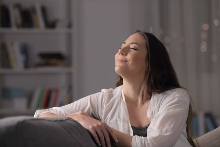 Happy woman breathing fresh air sitting on a couch in the night at home