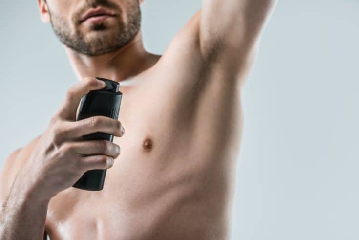 Cropped view of shirtless man spraying deodorant, isolated on grey