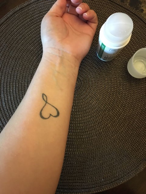 Person's arm with heart tattoo on the brown background with a bottle of bali deodorant