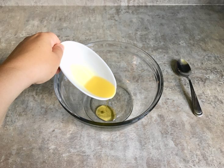 A closeup shot of a hand pouring an oil into the bowl, spoon on the side