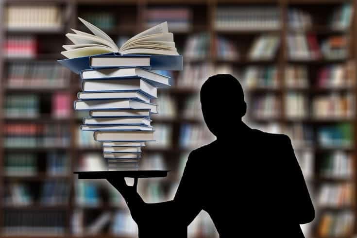 shadow of a man holding a pile of books on blurry library background