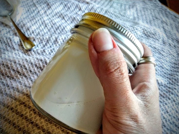 a close up shot of a person's hand holding a jar of DIY sunscreen