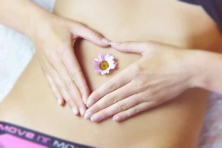 woman formed her hands a heart shape on her belly with a flower on her belly button
