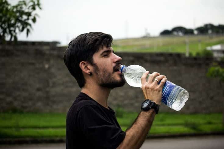 man in black shirt drinking water in the bottle in blurry green field background