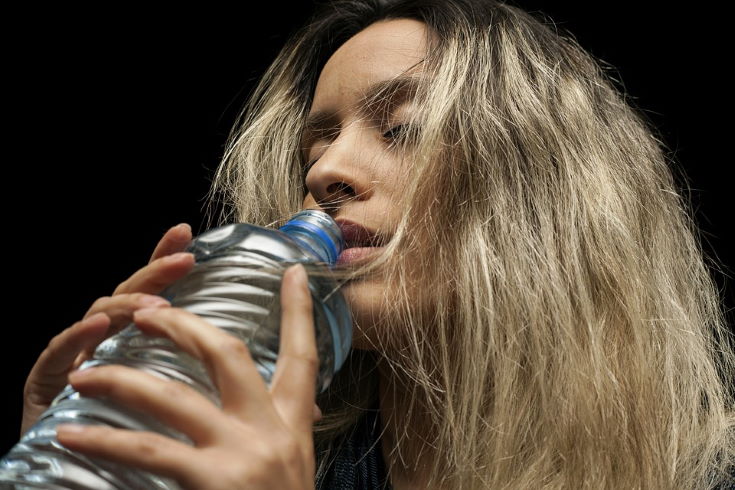 woman closing her eyes holding a bottled water close to her mouth