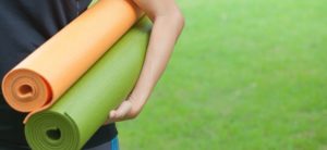 woman holding 2 yoga mat in green field background