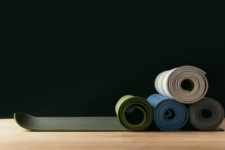 Different colored rolled yoga mats on wooden table