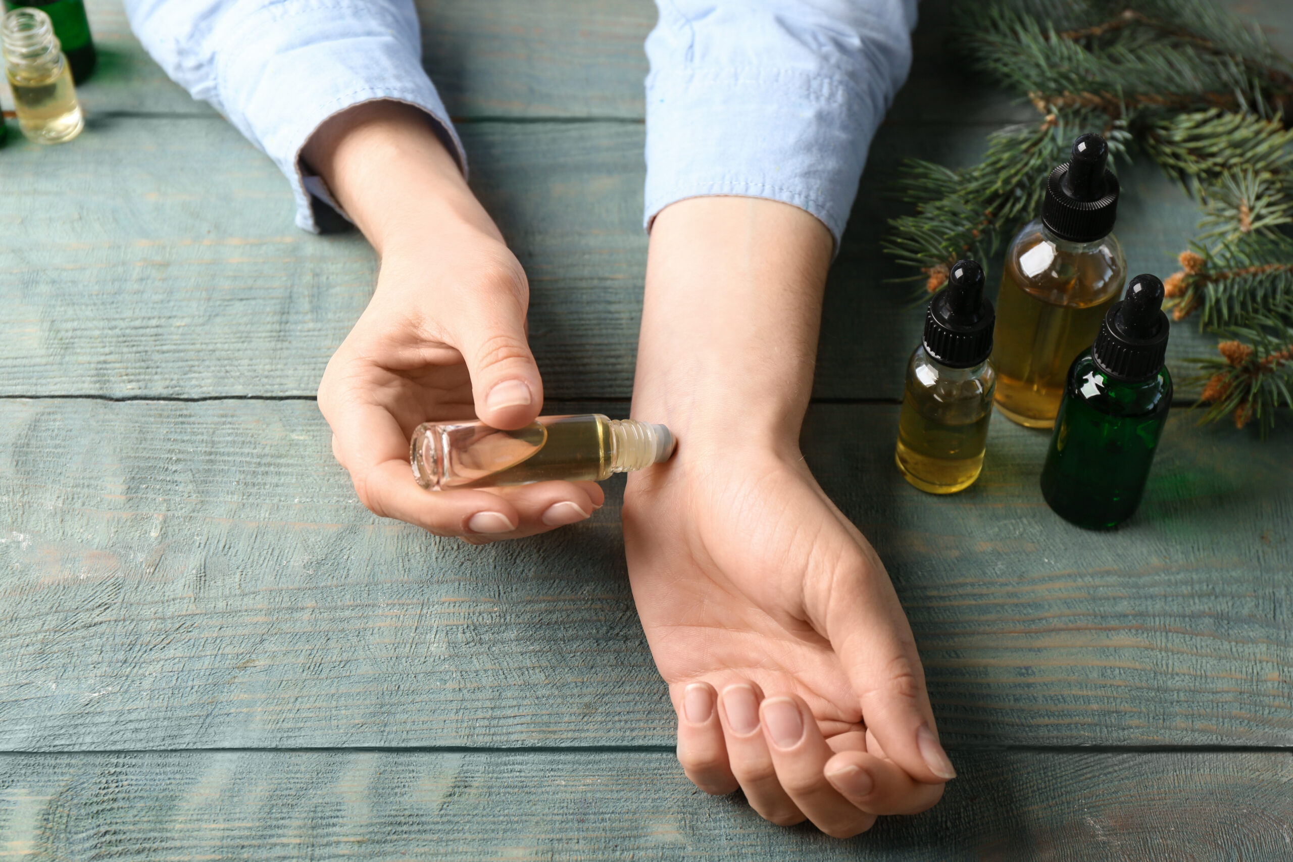 Woman applying essential oil on wrist at wooden table, closeup